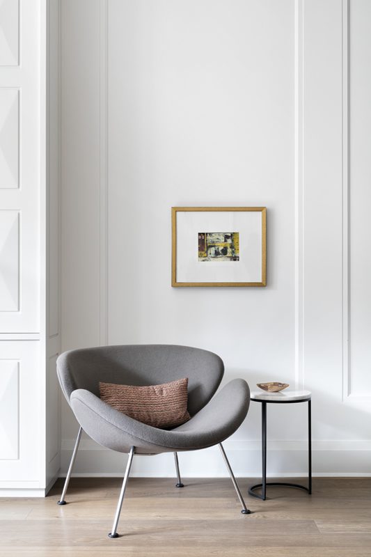 A grey chair sits in front of a white wall.