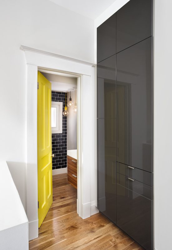 A hallway with a yellow door and black cabinets.