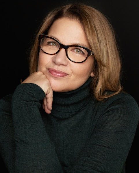 A woman in glasses posing with her hand on her chin.