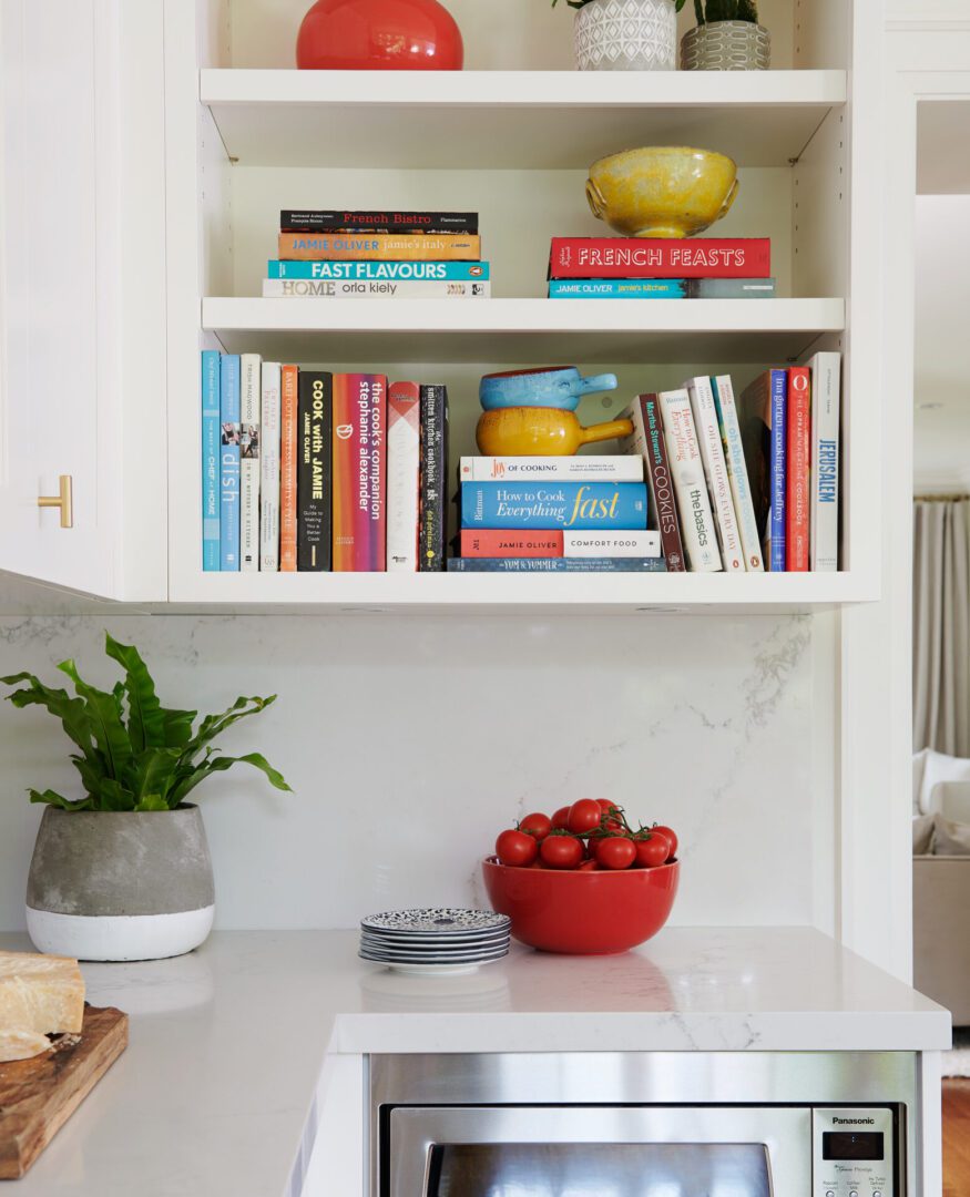 A kitchen with white cabinets and a red bowl of fruit.